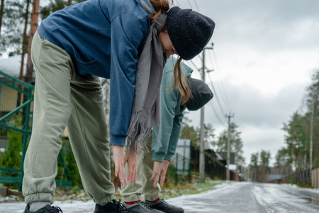 A teenage brother and sister challenge flexibility by bending forward, attempting to touch toes with...