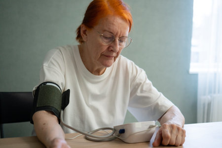 elderly woman in closeup view is closely watching the screen of her blood pressure monitor. vigilance and personal attention required for daily health tracking and hypertension control in senior yearsの写真素材