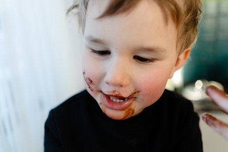 Close up portrait of a three year old boy with chocolate smeared all over his face. Sticky mess after eating. Concept of unhealthy eating, allergies, diabetes, and childhood obesity.の写真素材