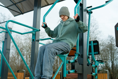 A girl performing arm press exercise on outdoor gym equipment, view from below. Daily routine of...