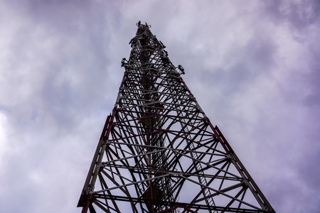 high voltage tower against grey sky with heave clouds. Steel construction view from below. metal pylons connect to horizontal vertical diagonal lines on tower as stairs to the skyの写真素材