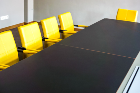 Bright yellow armchairs stands near black table in meeting room and wait for workers. The boardroom table is set for the Annual General Meetingの写真素材