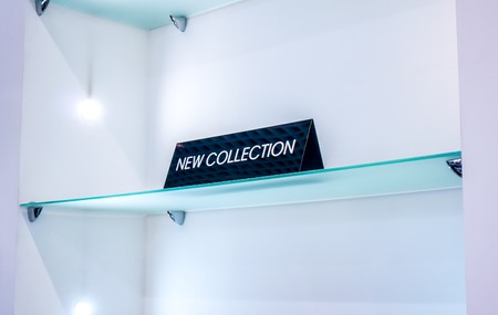medium tringle black plate in a clothing store with a sign NEW COLLECTION on grass shelf against...