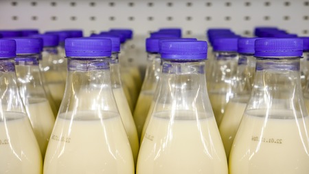 fresh organic milk in plastic bottles with bright dark blue round covers against metal background in the shop, bottles with milk as dairy product for preparing breakfast wait for byers on market shelfの写真素材