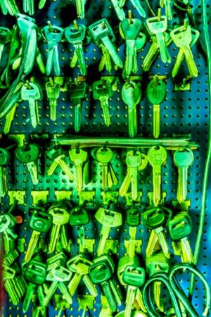 many small blank room keys hanging on a screw on a metal blue board in the workshop, part of the...