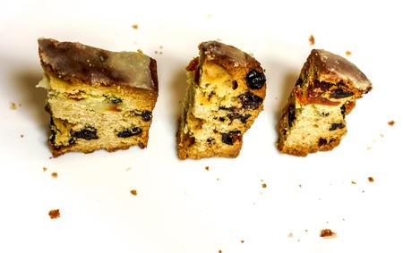 top view to three small peaces of holiday cake with raisins and other dried fruits surrounded by crumbs against white background. Christmas Stollen on a white plateの写真素材