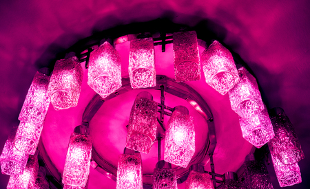 many bright crimson lamps of decorative modern shaped lamps on ceiling, crimson coral white lamps with light against dark background, many modern ceiling lamps with ornament, high quality resolutionの写真素材