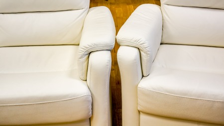 two white lather soft armchairs divided into sections for comfortable waiting on reception or in waiting room in big office. close up of white armchairs in big boss cabinetの写真素材