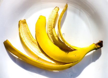 bright yellow banana skin without ripe inside lay on white plate as human five fingers. banana skin isolated on white background in sunshineの写真素材