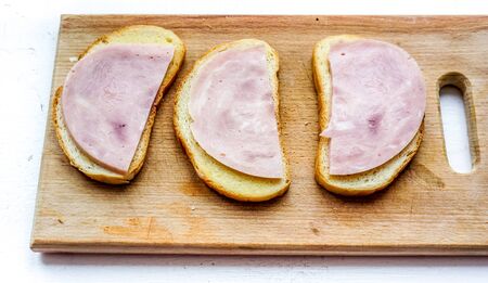 top view to wooden desk with three morning sandwiches made with white bred, some butter and thin peaces of sausage. sandwiches with ham as part of breakfastの写真素材