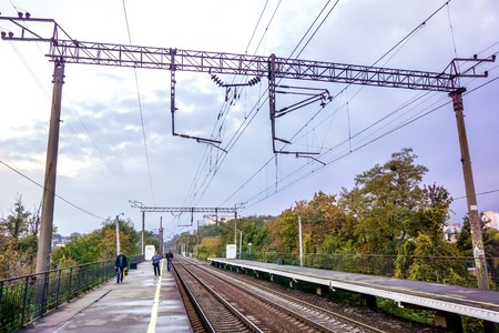 grey big clouds above empty railway station with grey broken asphalt and yellow line marking between green trees. Industrial landscape with railroad, colorful cloudy blue sky.の写真素材