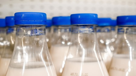 army of round blue covers with small vertical lines on plastic bottles with milk inside against...