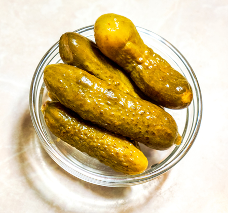 diagonal green different sizes cucumbers lay as vertical lines one by one on small glass deep plate against white background. Pickled green gherkins in round clean glass plateの写真素材