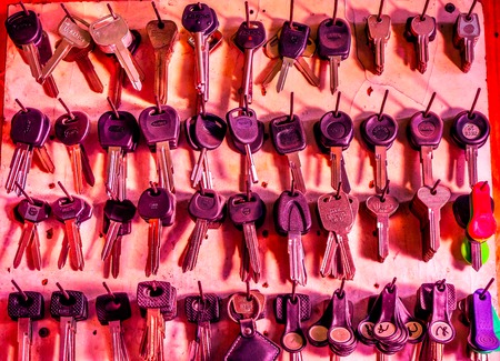 toned to red futute silver vintage keys hanging on a screw on a wooden brown board in the workshop,...