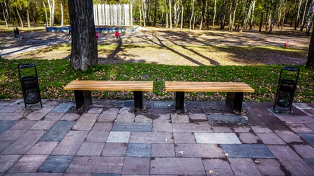 pair of two new strong wooden bench with metal legs stay on grey pawing stones near green meadow...