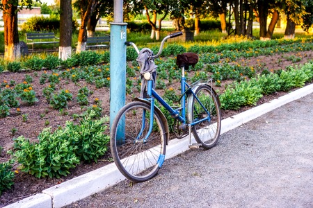 Blue women vintage old bicycle parcked near pylon against green grass and flowers. Retro vintage bicycle. Retro bicycle parked on the street. Vintage worn used red bicycle. Vintage effect.の写真素材