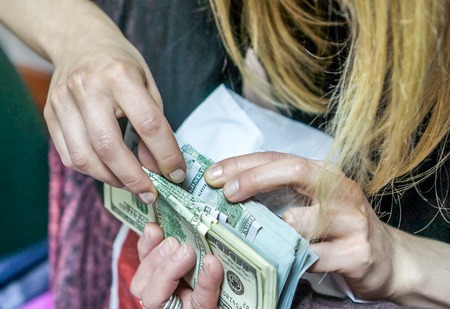 how to check dollar. dollar in hands. women or man ounts dollar bills and get it into the light ivory grey table. Pile of new and old one hundred dollar bills.の写真素材