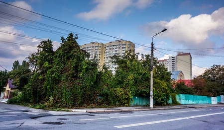 grey asphalt road with white lines as road marking between small houses, fences, parking cars and...