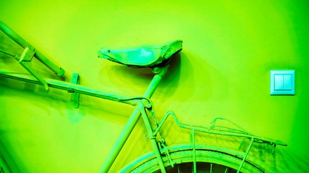 small light socket near acid green part of wheel, part of frame and saddle as part of old painted bicycle used for decoration in office. vintage bicycle on decorative color wall in art officeの写真素材