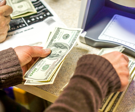 woman check bills on big white bill detector with violet light. woman hands took dollars into bill detector. New Dollar in the Money Detector in the Exchange Officeの写真素材