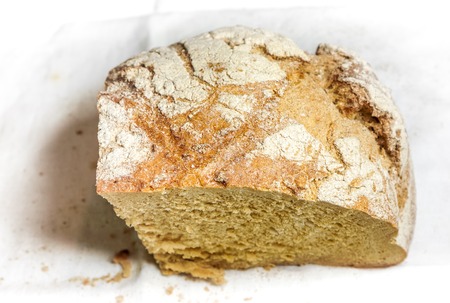 peace of big round homemade bread lay against white background. Bread with tears sprinkled with white flour against white country fabric. Bread as best symbol of food for people.の写真素材