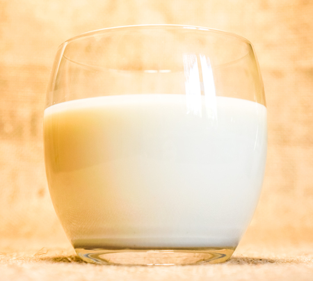 Side view of milk on classic country fabric background. fresh morning milk in clear glass against country fabric ivory brown background. morning organic milk glassの写真素材