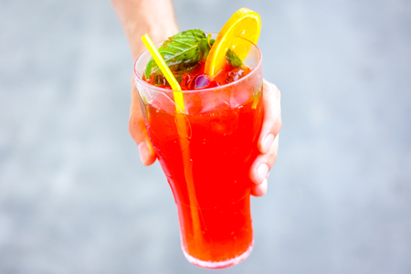 blurry effect on fresh cold red coral fruit watermelon strawberry mojito cocktail with mint, peaces of ice, slice of orange and strong cocktail tube against ivory grey background.の写真素材