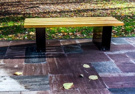 one new strong wooden bench with metal legs stay on grey pawing stones near green meadow with...