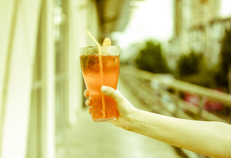 blurry effect on fresh cold red coral fruit watermelon strawberry mojito cocktail with mint, peace of ice, slice of orange and strong cocktail tube in strong man's hand against blurry city background.の写真素材