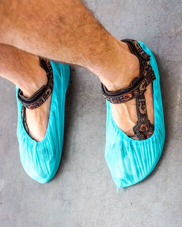 white skin man's legs in sandals with colorful overshoes against grey asphalt top view. Legs in plastic overshoes ready to go to clean room or premises.の写真素材