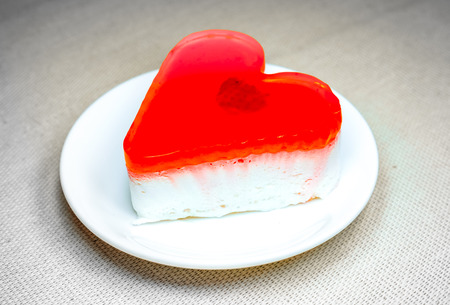 fresh red orange jelly heart cake with berry inside lay on round white plate. sweet jelly heart-shaped cakes on white concrete background. valentine's heart love cake. Free space for text.の写真素材