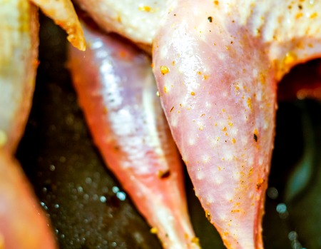 part of white skin raw quals with some spice frying on black teflon round pan with oil. five fresh raw meat on the board quail. future frying quals in sunshineの写真素材