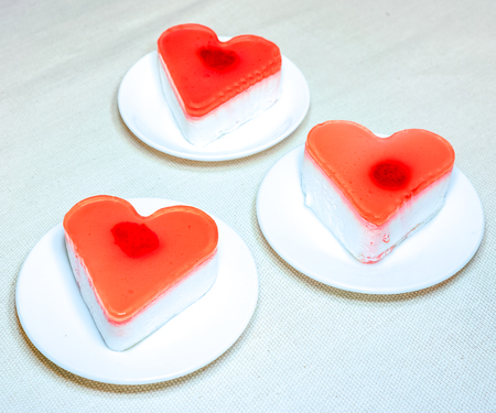 zigzag made by cakes. three sweet jelly heart cakes on white plates stand on pink table. parts of cakes on round plates. sweet jelly heart-shaped cakes on white concrete background. Free space for text.の写真素材