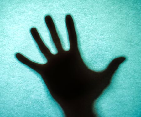 Mans hand as actor of shadow theatre. Hand's shadow as figure of Shadow hands of the Man behind frosted glass. Blurry hand abstraction. Halloween background. Black and white pictureの写真素材