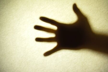 Mans hand as actor of shadow theatre. Hand's shadow as figure of Shadow hands of the Man behind frosted glass. Blurry hand abstraction. Halloween background. Black and white pictureの写真素材