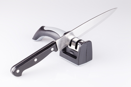 Knife and knife sharpener on a white surface. Kitchen tools isolated on white background.の写真素材