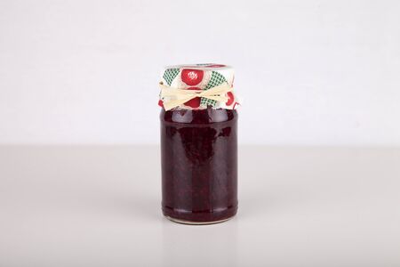 Jar of raspberry jam on a white surface. Jar of jam isolated on white background.