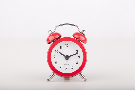 Replica of a vintage red bell alarm clock on a white surface. Alarm clock isolated on white...