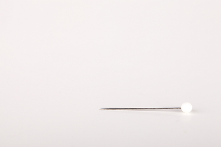 White straight pin on a white surface. White straight pin isolated on white background.の写真素材