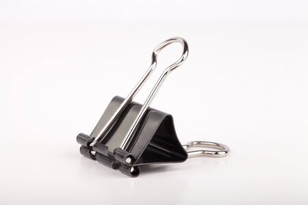 Black paper clip on a white surface. Black paperclip isolated on white background.