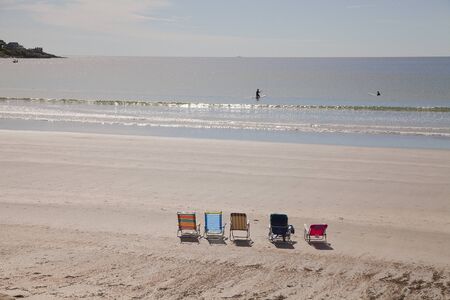 Chairs on the beach and swimmers in the ocean of York beach, USA.