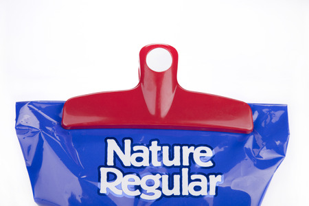 Red plastic chips bag clip on a blue bag of chips. Bag clip and chips bag isolated on white background.の写真素材