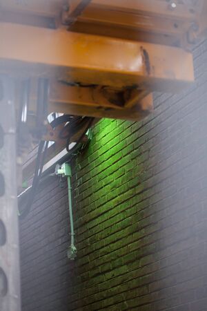 Yellow hoist and green LED light on a brown brick wall. Yellow painted beams of electric driven structure. Green LED light illuminating a brown brick wall.の写真素材
