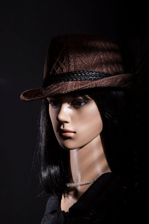 Plastic woman mannequin with brown hat posing for a low key film noir studio shoot on a black backgroundの写真素材