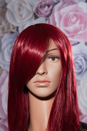 Plastic woman mannequin with long straigt red hair posing in front of a background with colorful rosesの写真素材