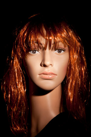 Red haired plastic woman mannequin with bright hair posing on a black backgroundの写真素材