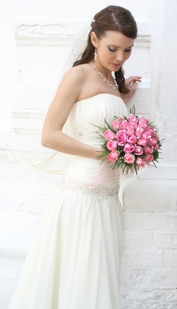 A lovely bride looks down at her bouquet from roses  She is dressed in a simple gown and wearing a veil の写真素材
