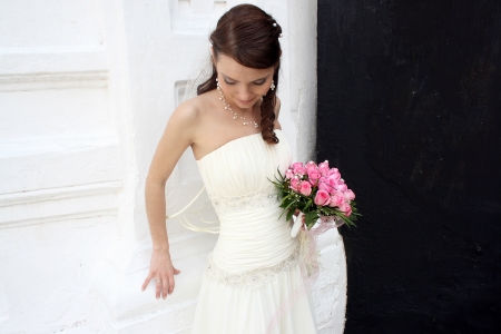 A lovely bride looks down and hold her bouquet from roses  She dressed in a simple gown and wearing a veil  Contrast background - black and white の写真素材