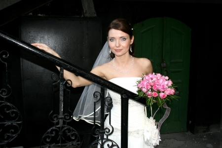 A lovely bride with bouquet from roses on black stairs  Green door behind her の写真素材