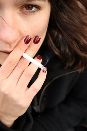 A girl with red nails smoking a cigarette. Close up of a young woman.の写真素材